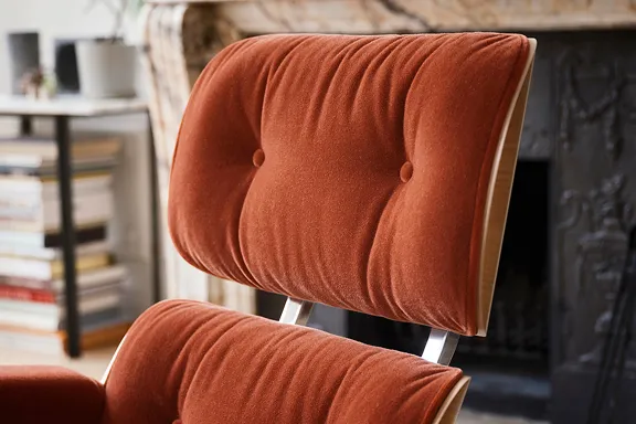 Nahaufnahme eines Eames Lounge Chair in Rostrot mit hellem Holz, Marmorkamin und Bücherstapel.